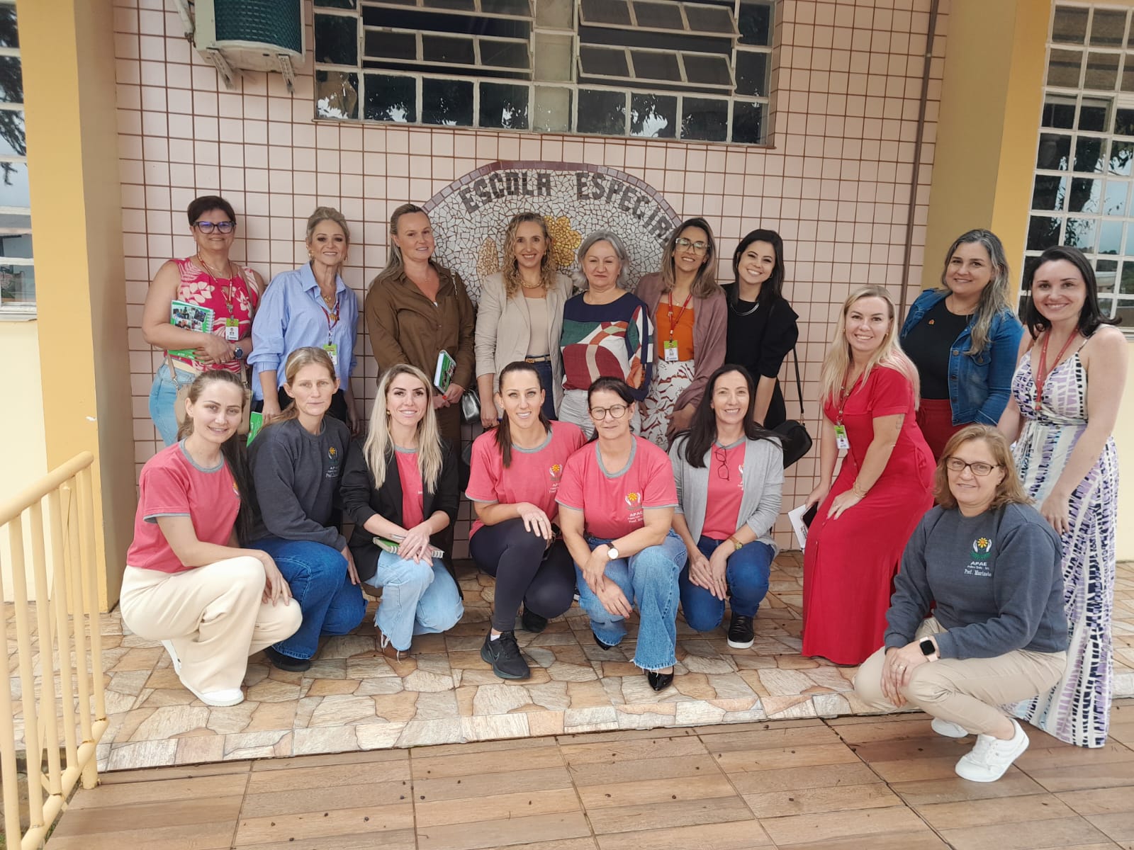 Um grupo de dezesseis mulheres posam para uma foto. Todas são brancas e estão na entrada de uma escola, da cor creme. A equipe de trás está em pé, enquanto as mulheres da frente estão agachadas. Ao fundo aparece uns dizeres com o nome em pedras de azulejos "Escola Especial".