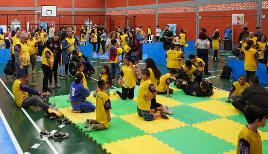 Crianças na edição 2023 do Festival Paralímpico na FCEE crianças com camisetas amarelas em ginásio, tatames verde e amarelo