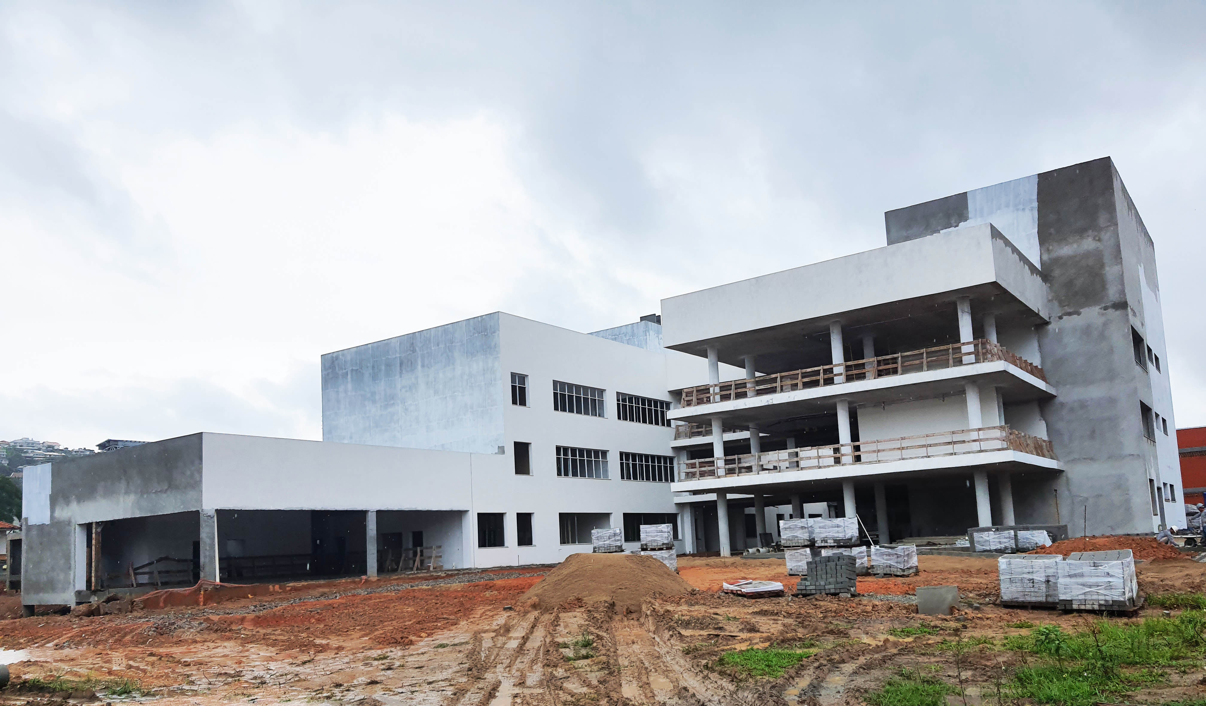 Obra do novo prédio da FCEE no dia 18 de janeiro de 2024 Edifício de 3 andares em obra, pintado parcialmente de branco, terra no chão