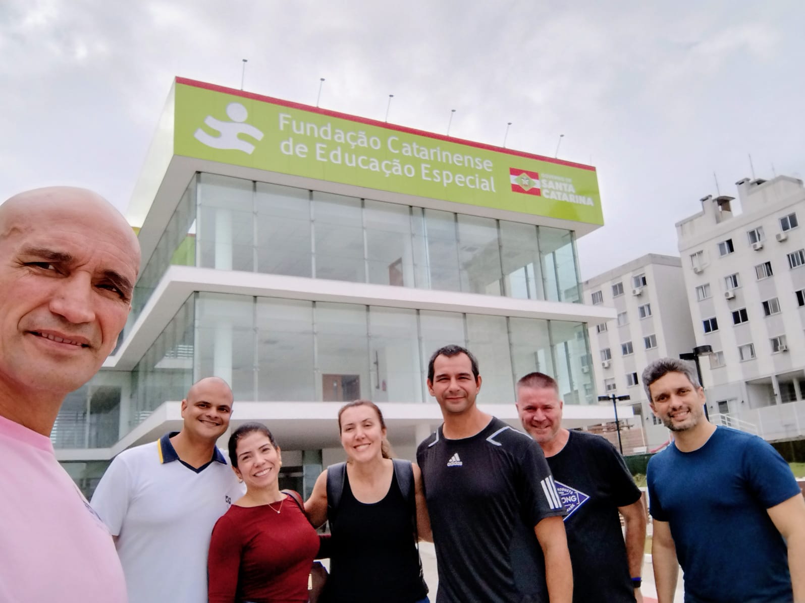 Sete pessoas posam para foto, ambiente aberto, ao fundo prédio novo da FCEE